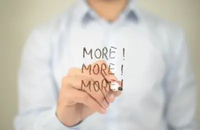 man in dress shirt writing more, more, more on a board