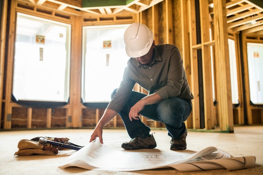 man wearing hard hat looking at blueprints on job site