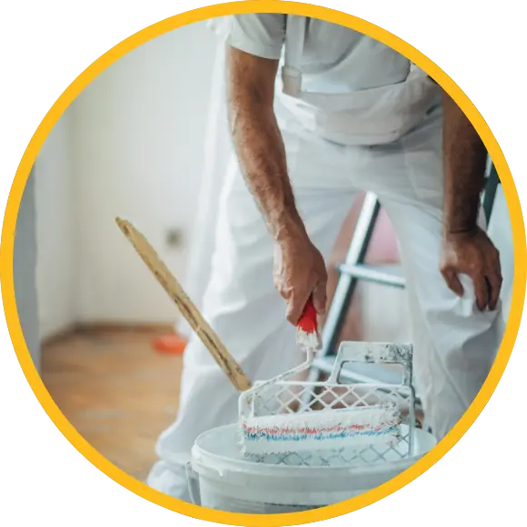 painter with roller leaning over paint bucket